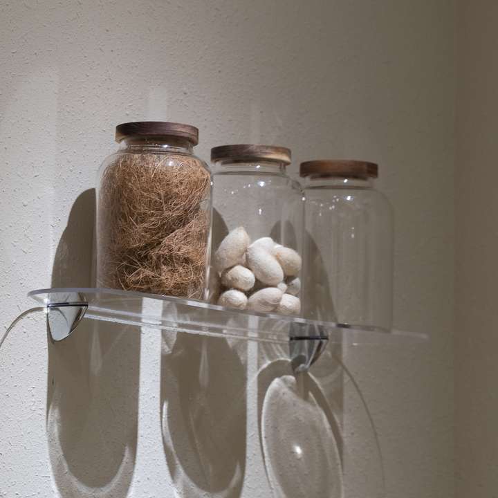 Glass jars of silk cocoons and raw fibre on a clear acrylic shelf